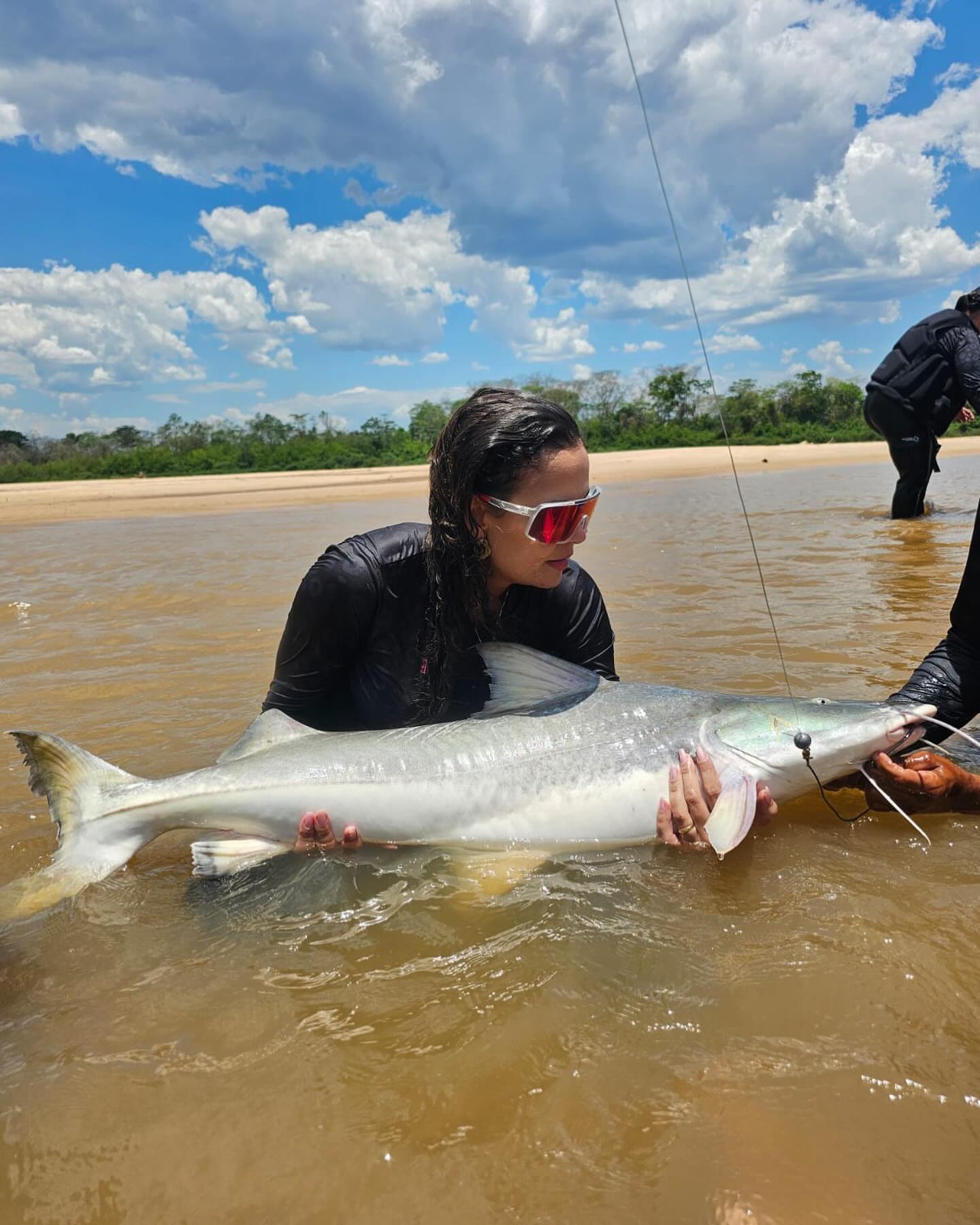 Pescadora ajoelhada na água ao lado de um peixe